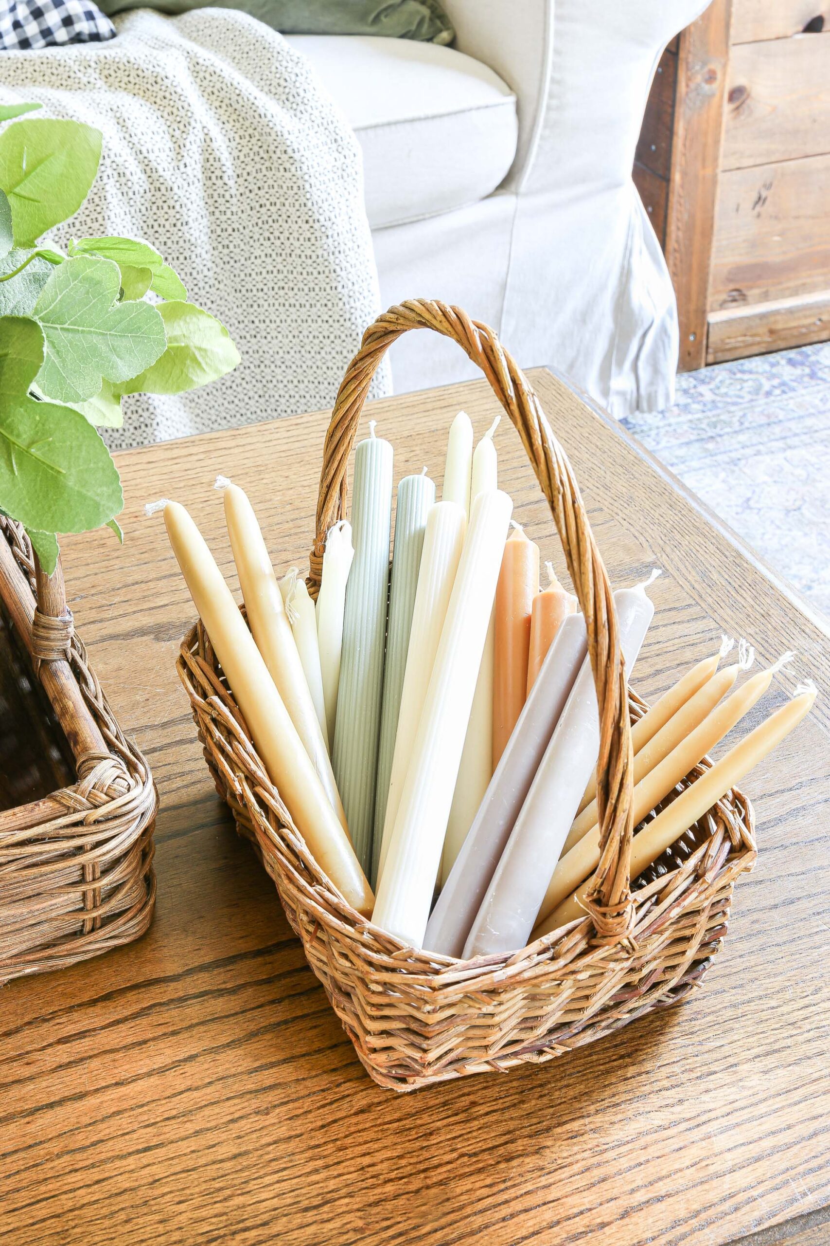 A small wicker basket with handle carrying many different kinds and colors of taper candles.
