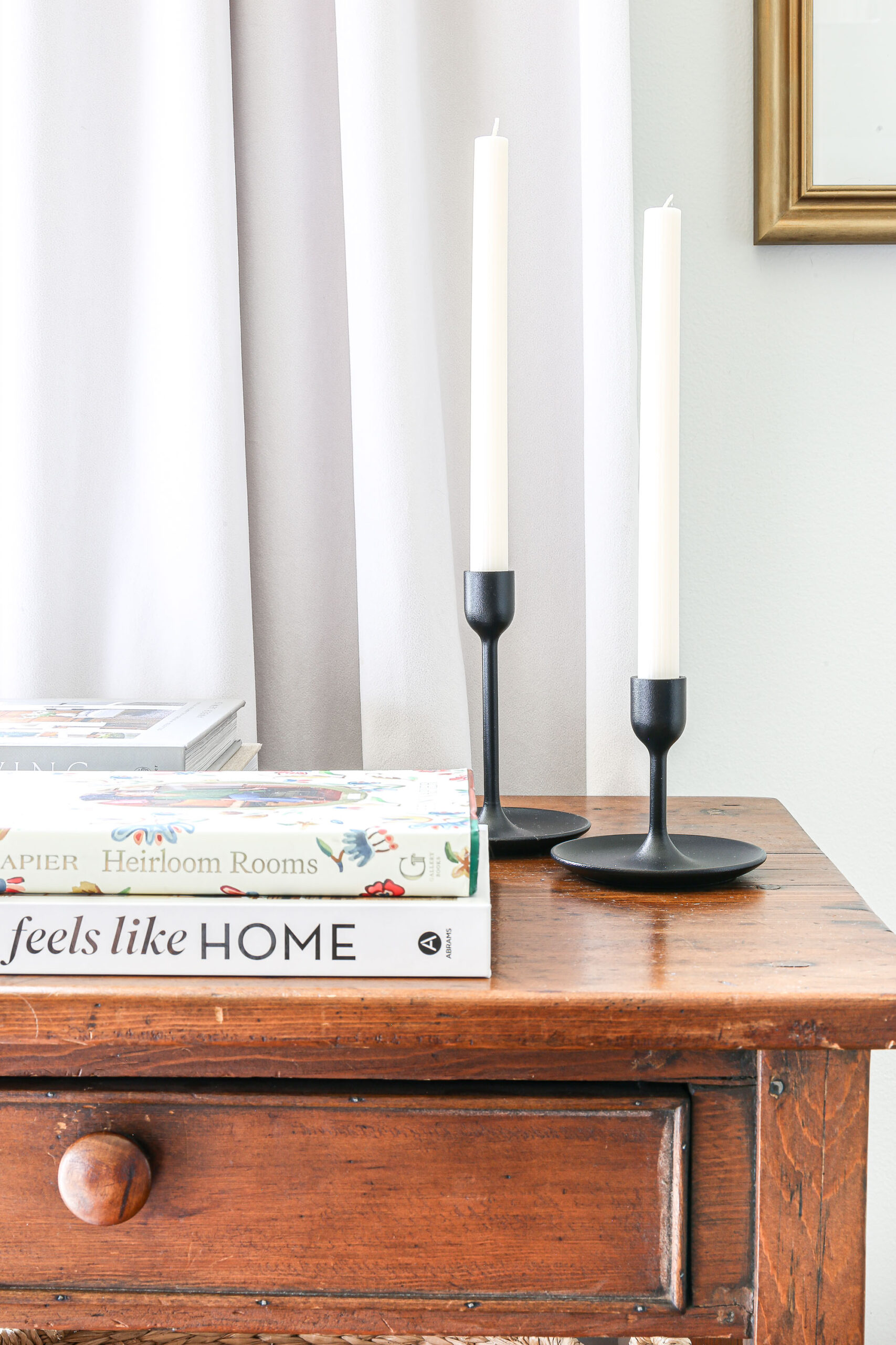 Two ribbed white taper candles in two back candlestick holders on an antique side table.